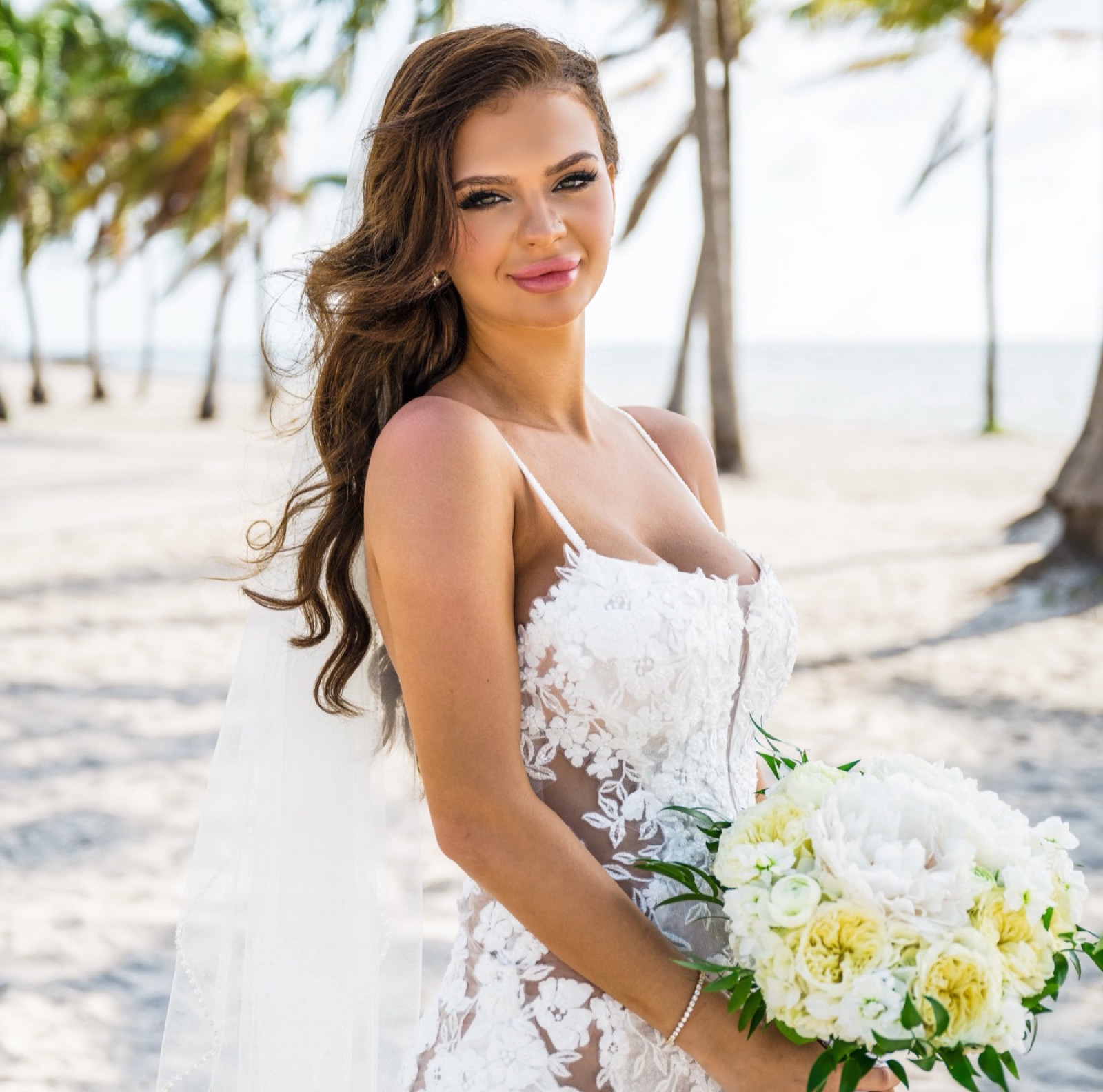 Bride with bouquet under palm trees wearing a Sunkiss Studios bridal spray tan on her wedding day